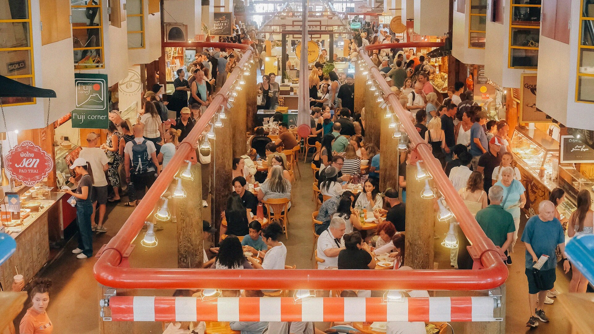 Busy Granville Island Public Market with crowds dining at communal tables under hanging warehouse lights in Vancouver