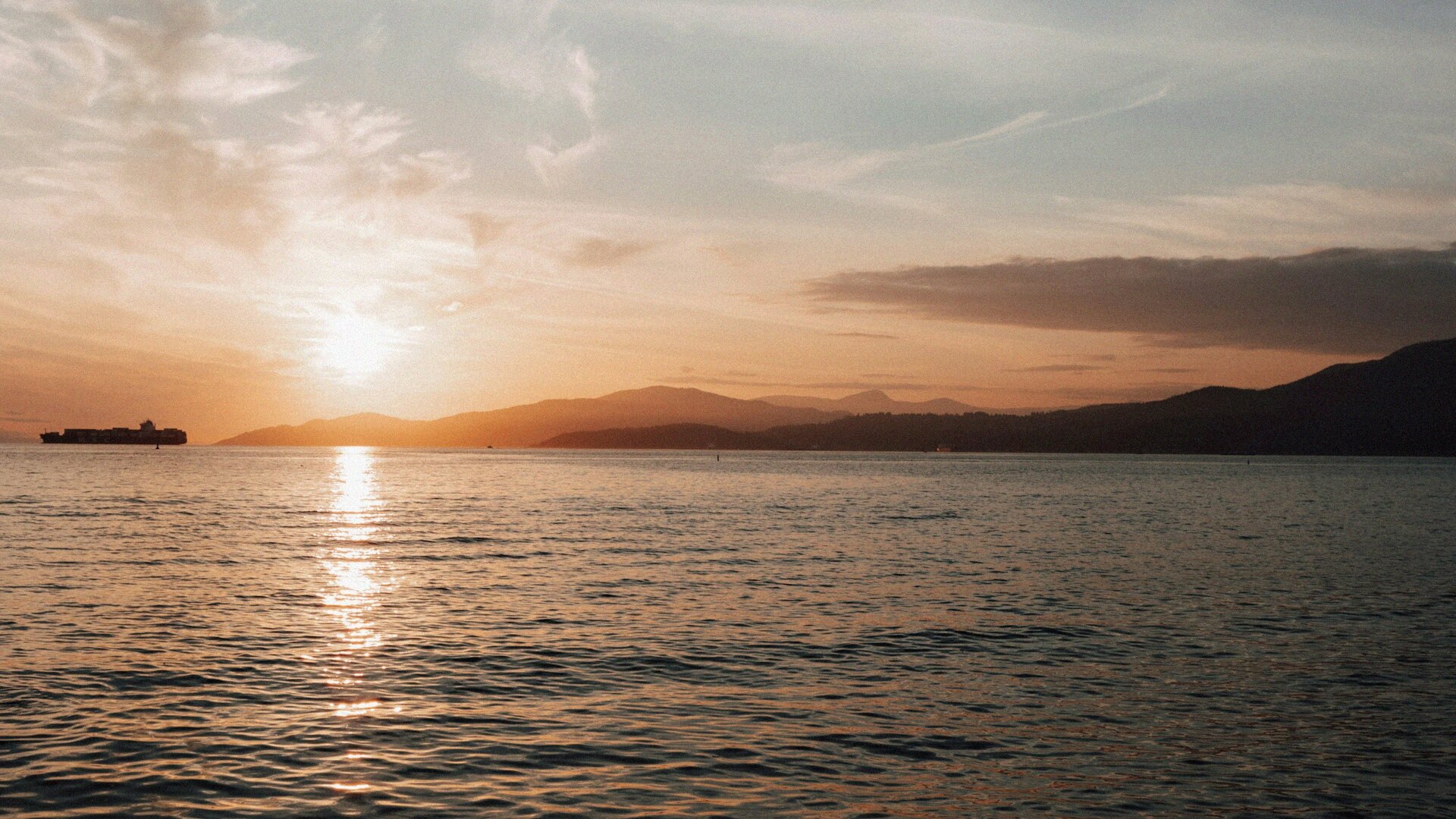 Pacific Ocean at golden hour with a container ship on the horizon and the silhouetted mountains of the Sunshine Coast in the distance